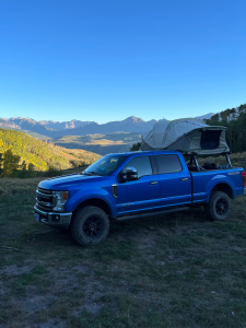 A blue truck with rooftop tent sitting in front of mountain background.